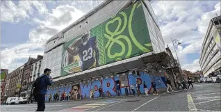  ?? KENNETH MAGUIRE/ASSOCIATED PRESS ?? A pedestrian crosses Dame Street — renamed “Notre” Dame Street for the weekend — below a giant Notre Dame football mural Friday in Dublin, Ireland. The Fighting Irish play Navy today at Aviva Stadium, with a portion of the street closed to traffic to become a fan zone.