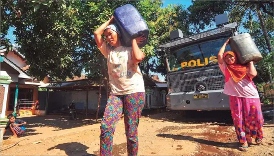  ?? RENDRA KURNIA/JAWA POS RADAR BANYUWANGI ?? TUGAS EKSTRA MOBIL WATER CANNON: Warga Dusun Pancoran, Desa Sidowangi, Wongsorejo, Banyuwangi, memanggul jeriken yang telah diisi air bersih oleh Satuan Sabhara Polres Banyuwangi kemarin.