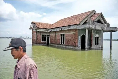  ?? AP PHOTO/DITA ALANGKARA ?? In 2021, a man walks past a house abandoned after it was inundated by the rising sea level in Sidogemah, Central Java, Indonesia.