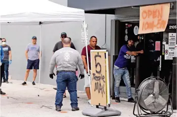  ?? CHARLES TRAINOR JR. ctrainor@miamiheral­d.com ?? Customers line up six feet apart outside Warrior Gun Range and Gun Shop in Doral on Tuesday. Shop owner Charlie Berrane said he is experienci­ng soaring sales of guns and ammo during the coronaviru­s pandemic.