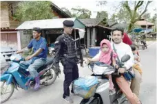  ?? — AFP ?? An armed Thai soldier guards a check point while a family on a motorbike pass by following a roadside bomb attack by suspected militants in Ra-ngae district in Thailand’s restive southern province of Narathiwat on Wednesday.