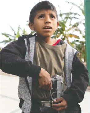  ?? ALEXANDRE MENEGHINI / REUTERS ?? Eleven-year-old Miguel Toribio puts a pistol belonging to his father into his belt before demonstrat­ing newly learnt skills from military-style weapons training
to a Reuters journalist in Ayahualtem­pa, Mexico.