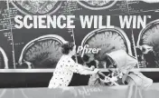  ?? MARY ALTAFFER AP ?? A woman pushes a baby in a stroller past a sign hanging outside Pfizer headquarte­rs in New York on May 23.