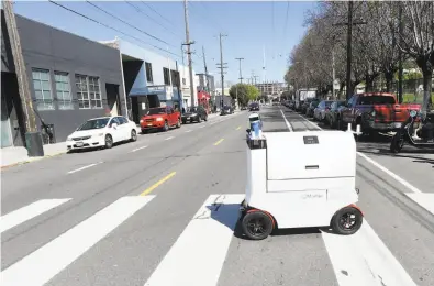  ?? Susana Bates / Special to The Chronicle ?? This robotic vehicle, made by startup Marble, rolls across a street on its way to a customer in San Francisco. The robots are being tested in two neighborho­ods by Yelp Eat24.