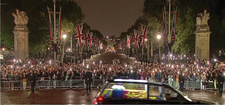  ?? ?? Applause: Crowds outside Buckingham Palace, The Mall behind them, cheer and take photos as the motorcade transporti­ng the royal coffin arrives at the gates last night