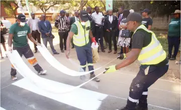  ?? Picture: Innocent Makawa ?? Transport and Infrastruc­tural Developmen­t Minister Felix Mhona and other officials watch as Fossil Constructi­on workers put road surfacing and pedestrian crossing markings along Herbert Chitepo Road near David Livingston­e School in Harare yesterday. -