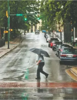  ?? STAFF PHOTO BY DOUG STRICKLAND ?? A pedestrian crosses Sixth Street at Market Street after Tropical Storm Cindy brought rainfall to the region on Thursday. Rain is expected to continue through Saturday.