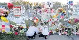  ?? GERALD HERBERT/AP ?? People light candles at a makeshift memorial outside Marjory Stoneman Douglas High School in Parkland on Feb. 18, 2018, where 17 students and faculty were killed in a mass shooting days earlier.