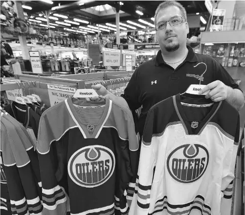  ?? JOHN LUCAS/ EDMONTON JOURNAL ?? United Cycle employee Darren Odynski holds some Edmonton Oilers jerseys at the southside store on Thursday.