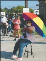  ?? (AP/Russ Bynum) ?? Crystal Clark sits on a folding stool while holding an umbrella for shade as she waits in line to vote early. Clark arrived at the polls prepared for a long wait in line.