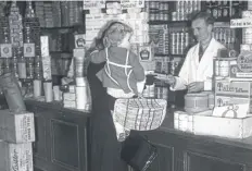  ?? ?? A housewife hands over her ration books to a grocer after rationing of bacon, sugar and butter began today in 1940