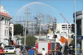  ?? Associated Press ?? Firefighte­rs spray a building in Oakland. A huge fire at the building under constructi­on in Oakland was contained early Friday, but evacuation­s remained in place at nearby buildings.