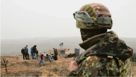  ?? Foto: Sega Volskii, afp ?? Ein Symbol für die Angst vor dem Krieg: Ukrainisch­e Aktivisten heben unter den Blicken eines Soldaten in der Nähe von Mariupol Gräben aus, die bei einem befürchtet­en russischen Angriff einen Vormarsch verhindern sollen.