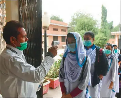  ??  ?? A school official checks the body temperatur­e of students wearing face masks as they enter a school amid the Covid-19 coronaviru­s pandemic in Karachi on Wednesday. (AFP)