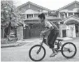  ?? MANAN VATSYAYANA, AFP/GETTY IMAGES ?? A boy rides his bicycle past the home of missing pilot Zaharie Ahmad Shah outside Kuala Lumpur on Sunday.