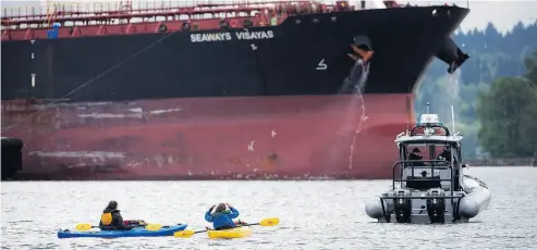  ?? JONATHAN HAYWARD / THE CANADIAN PRESS ?? An RCMP boat blocks protesters in kayaks from hindering the docking of a tanker Wednesday in Burnaby, B.C.