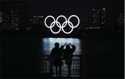  ?? EUGENE HOSHIKO ?? FILE - In this Dec. 1, 2020, file photo, a man and a woman look at the Olympic rings float in the water in the Odaiba section in Tokyo. Tokyo Olympic organizers are expected to unveil their fifth annual budget before Christmas.