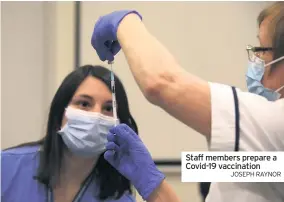  ?? JOSEPH RAYNOR ?? Staff members prepare a Covid-19 vaccinatio­n