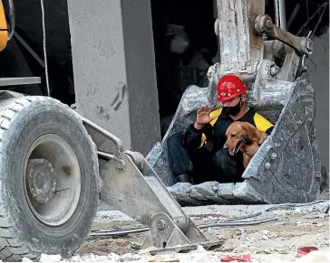  ?? AP ?? A rescue worker and his search dog are transporte­d on the shovel of an earthmover to search for survivors at the site of a deadly explosion that destroyed the five-star Hotel Saratoga in Old Havana.