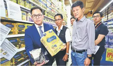  ??  ?? Dr Cheong (left) showing a packet of milk powder which was checked during the inspection. Also seen is Yong (second right). — Photo by Muhammad Rais Sanusi