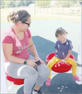  ??  ?? Dalia Manjarrez and her daughter, Maddie, 3, try out one of the seats at the new playground at Creekside Park in Farmington.