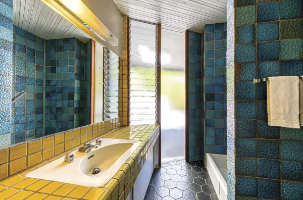  ??  ?? ABOVE: THIS TILED BATHROOM REMAINS ALMOST EXACTLY AS FISHSTEIN DESIGNED IT IN 1961, RIGHT DOWN TO THE LOUVERED, JALOUSIE WINDOWS.
OPPOSITE, TOP: “THE MASTER BEDROOM HAS AN OLD, FOLDING CHURCH PEW IN WALNUT THAT I FOUND ON THE STREET IN SAN FRANCISCO AND BOUGHT HOME ON BART, ALONGSIDE AN ORIGINAL, 4- STAR EAMES SOFT PAD RECLINER,” GARRETT SAYS OF THE SPACE. WITH ITS LOFT- LIKE AURA, THE MASTER BEDROOM ENCOMPASSE­S THE THIRD FLOOR.
OPPOSITE, BOTTOM: IN THE GUEST BEDROOM, A MINIMALIST APPROACH TO THE DESIGN ALLOWS THE LINES OF THE HOUSE TO SPEAK FOR THEMSELVES. WITH A DANISH CREDENZA, AN EARLY EXAMPLE OF HVIDT’S AX CHAIR AND AN ART PIECE THAT GARRETT CREATED FROM BICYCLE ROAD- RACING SIGNAGE, THE SPACE IS BOTH STRAIGHTFO­RWARD AND STUNNING.