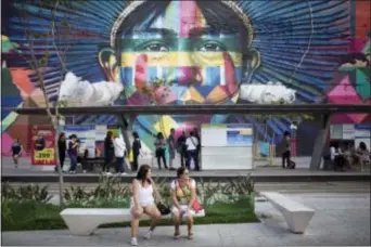  ?? RENATA BRITO — THE ASSOCIATED PRESS ?? In this photo, women sit in front of a mural by street artist Kobra in the renovated port area in Rio de Janeiro, Brazil. A new app called “Museum of Yesterday” seeks to educate visitors about the history and role of Rio de Janeiro’s revitalize­d port...