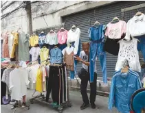  ?? REUTERS ?? A STREET VENDOR peers through clothes he is selling as police sweep through a street in Bangkok, Thailand in this Sept. 12 photo.