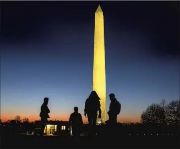  ?? Kent Nishimura Los Angeles Times ?? PEOPLE WALK on the National Mall with the Washington Monument illuminate­d in the evening sky, nearly a week after a mob breached the security of the nation's Capitol. An impeachmen­t vote is set for Wednesday.