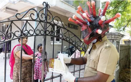  ?? AFP ?? A policeman wearing a a coronaviru­s helmet distribute­s pamphlets to raise awareness about the COVID-19 at a residentia­l area in Chennai on Sunday.