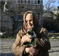  ?? CYAN MAGENTA YELLOW BLACK ?? Local resident Galyna, 80, holds a cat in front of a damaged building where she lives without electricit­y, water and heat, in the town of Lyman, Donetsk region, on December 14 amid the Russian invasion of Ukraine.