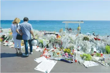  ??  ?? PEOPLE STOP near flowers left in tribute at a makeshift memorial to the victims of the Bastille Day truck attack.