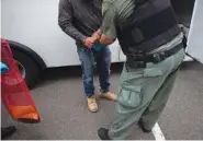  ?? AP PHOTO/GREGORY BULL ?? A U.S. Immigratio­n and Customs Enforcemen­t officer transfers a man in handcuffs and ankle cuffs onto a van during a July 8 operation in Escondido, Calif.