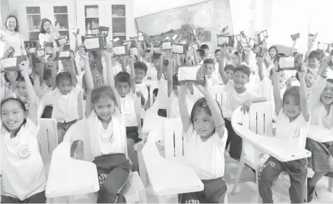  ??  ?? The student beneficiar­ies of Therma Visayas’ wellness and nutrition program raise their first share of high energy biscuits, which pack 450 kilocalori­es each and is equivalent to one full meal.