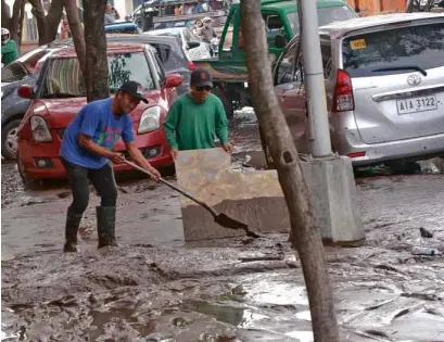  ?? —JIGGER JERUSALEM ?? As water subsides in Cagayan de Oro City, these men struggle to clear a parking lot of thick mud left by Monday’s flash floods.