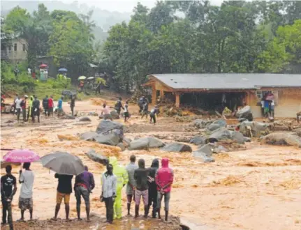  ?? Saidu Bah, AFP ?? People look on as floodwater­s rage past a damaged building Monday in Freetown, Sierra Leone. More than 300 people died as landslides struck the capital of the west African nation.