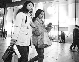  ?? NG HAN GUAN/AP ?? Shoppers walk past a store of US tech giant Apple in a retail district in Beijing on Friday.