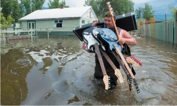  ?? CP PHOTO ?? Resident Lars Androsoff carries his friend’s guitars as he walks through the floodwater­s in Grand Forks on Thursday.