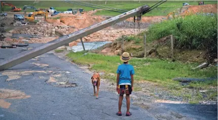  ?? RAMON ESPINOSA/AP ?? A boy accompanie­d by his dog watches repairs to Guajataca Dam in Quebradill­as, Puerto Rico, in 2017.