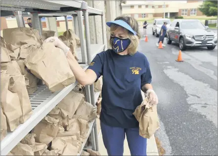  ?? BEN HASTY— READING EAGLE ?? Joan Sandritter, a cafeteria worker for the Muhlenberg Township School District, gets grab- and- go breakfasts and lunches from a rack to distribute them to families who drive up Sept. 10. The program has been going on since the start of the COVID- 19pandemic and is continuing this school year as all education in the district is being done virtually.