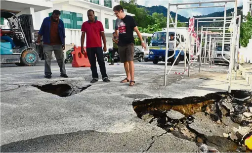  ??  ?? Hole-some neighbourh­ood: Dennis (centre) and his neighbours standing near the sinkholes outside his house in Tingkat Kelicap, Sungai Ara, Penang.