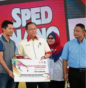  ??  ?? All smiles: Ismail Sabri (in white) presenting a mock cheque for RM10,000 to Mohamad Shah Riza Maarof, a recipient of the SPED programme during the launch at Laman Kerayong Bera. — Bernama