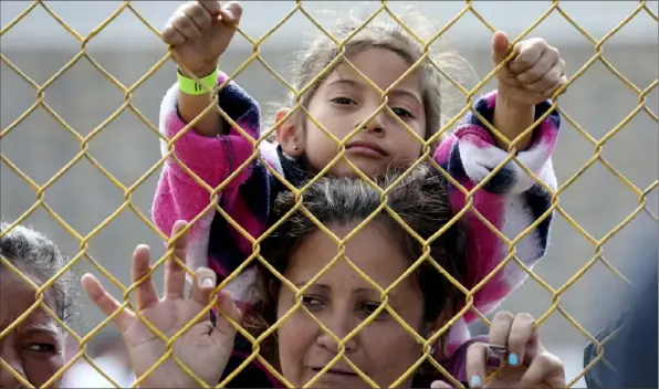  ?? Jerry Lara/The San Antonio Express-News via AP ?? Six-year-old Daniela Fernanda Portillo Burgos sits on the shoulders of her mother, Iris Jamilet, 39, as they look out through the fence of a immigrant shelter Tuesday in Piedras Negras, Mexico.