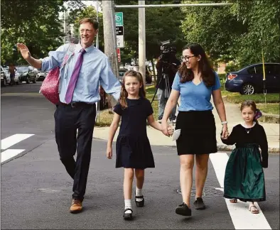  ?? Photos by Arnold Gold / Hearst Connecticu­t Media ?? New Haven Mayor Justin Elicker, left, and his wife, Natalie, walk their daughter, Molly, 7, center, to the bus stop on Orange Street in New Haven joined by her sister, April, 4, on the first day of school in the city Monday.