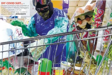  ??  ?? A shopper purchasing daily essentials at a supermarke­t in Marang, Terengganu using a makeshift covid suit comprising rubbish bags in a bid to prevent infection. – BERNAMAPIX