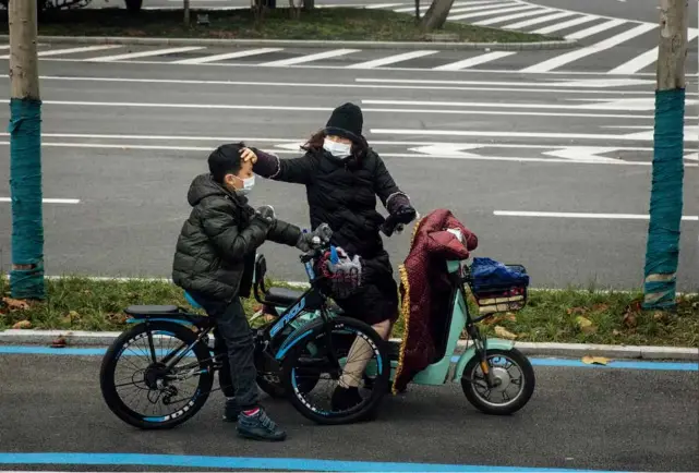  ?? 摄影 无畏 ?? 2020年1月27日，武汉市区，一位母亲暂时结束骑行­停靠路边，关心地触摸儿子的额头。