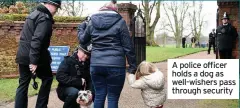  ??  ?? A police officer holds a dog as well-wishers pass through security