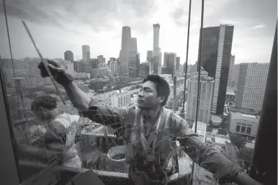  ?? Associated Press ?? ■ Chinese workers clean a window at an office building Friday in the scenic of Central Business District in Beijing.