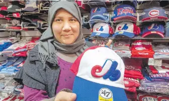  ?? CP ?? Karina Benami sells Expos baseball caps Thursday at Montreal’s Jannat Souvenir shop. Fourteen years after the major-league franchise left town, a group of investors says a new team would be viable.