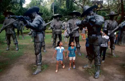  ?? ARNOLD ALMACEN ?? UNDER THE GUN Two girls gaze at the statues representi­ng the Spanish firing squad that executed Rizal at Bagumbayan 117 years ago.